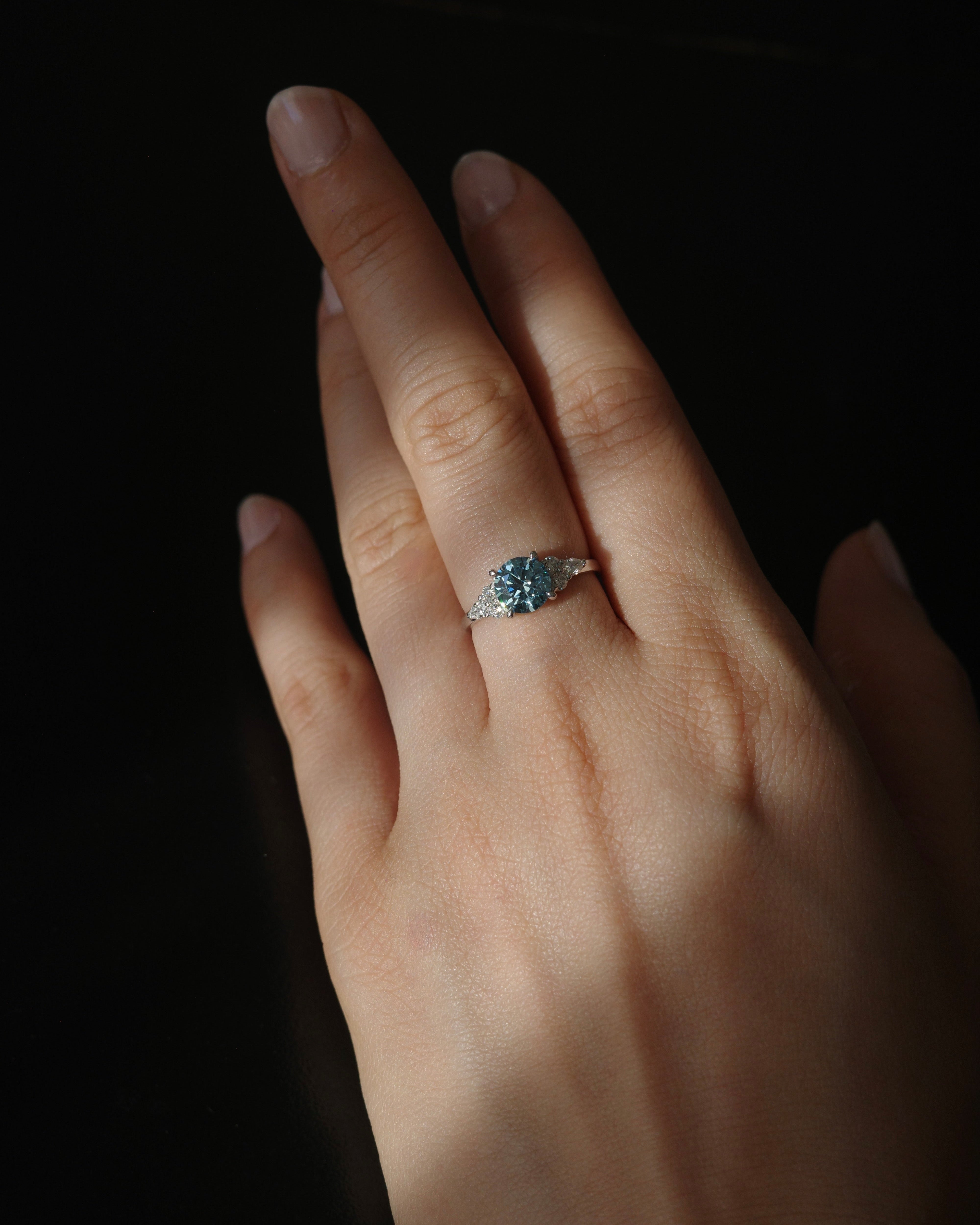 Hand wearing a ring with a blue gemstone against a dark background