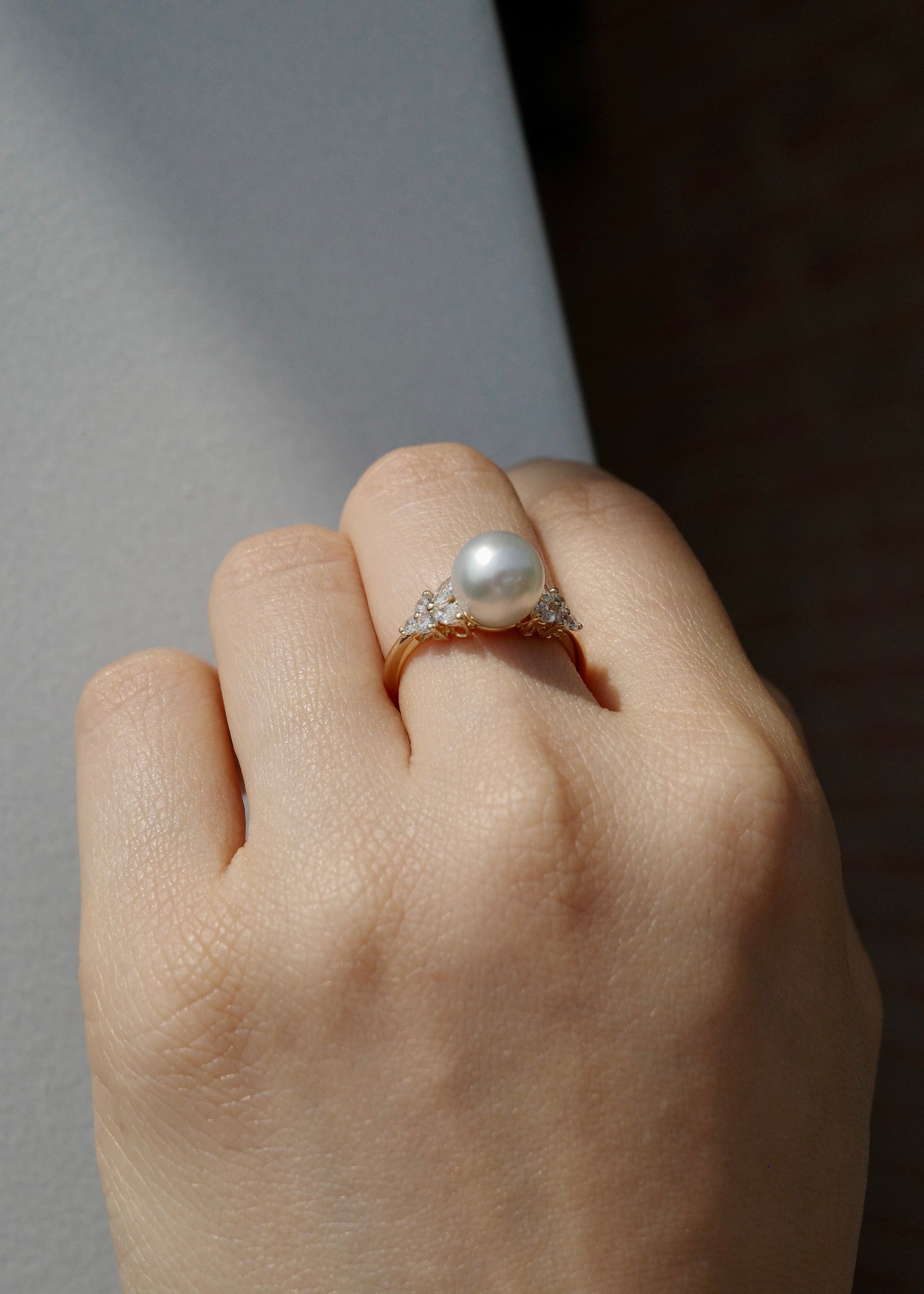 Hand wearing a pearl ring on a neutral background