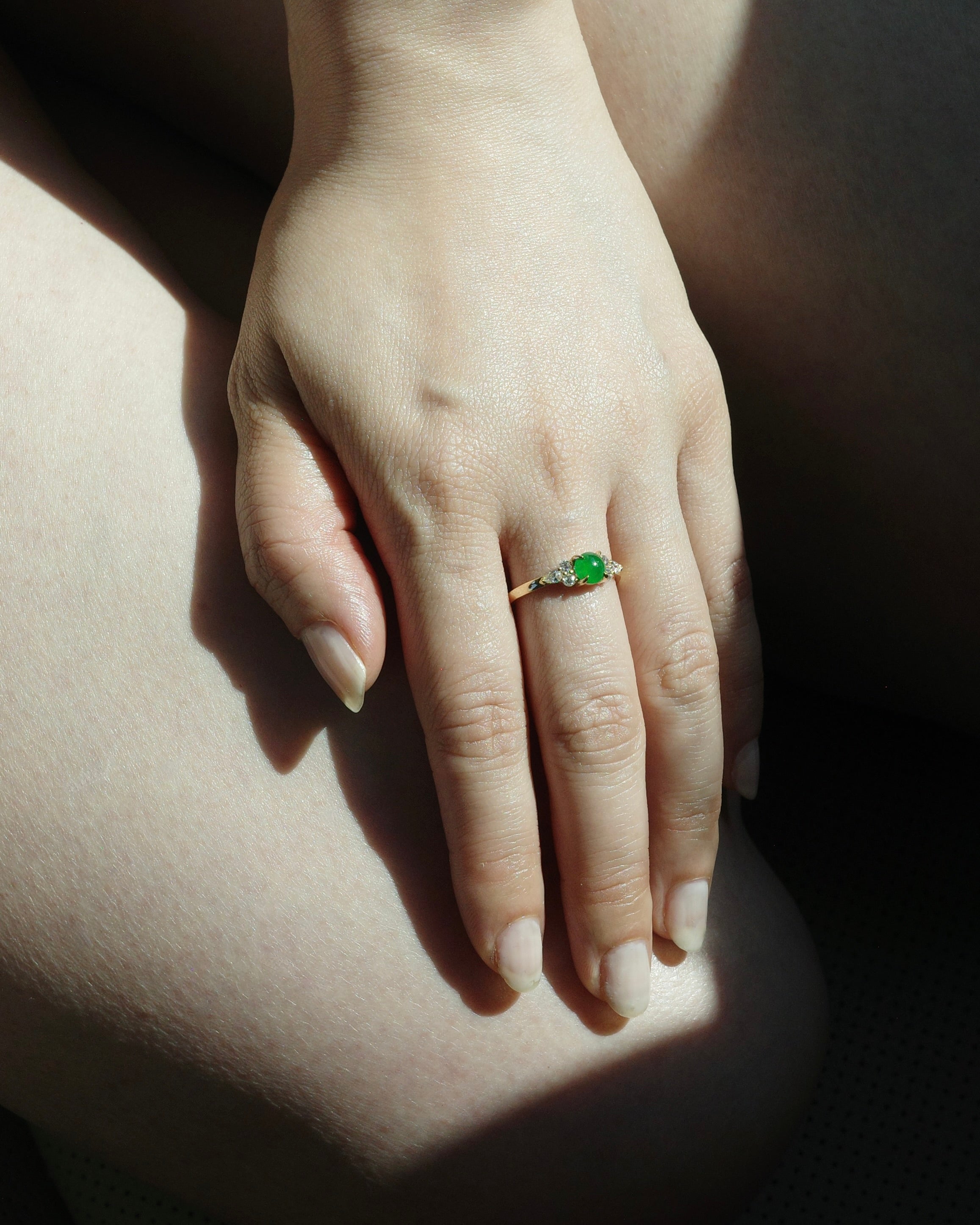 Hand wearing a 5mm natural green jade and diamonds ring on a light background