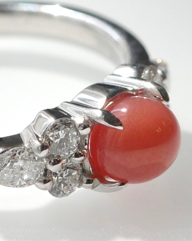 A white gold ring featuring a round, red natural conch pearl and pear diamonds and round brilliant cut diamonds, shown on a white background.