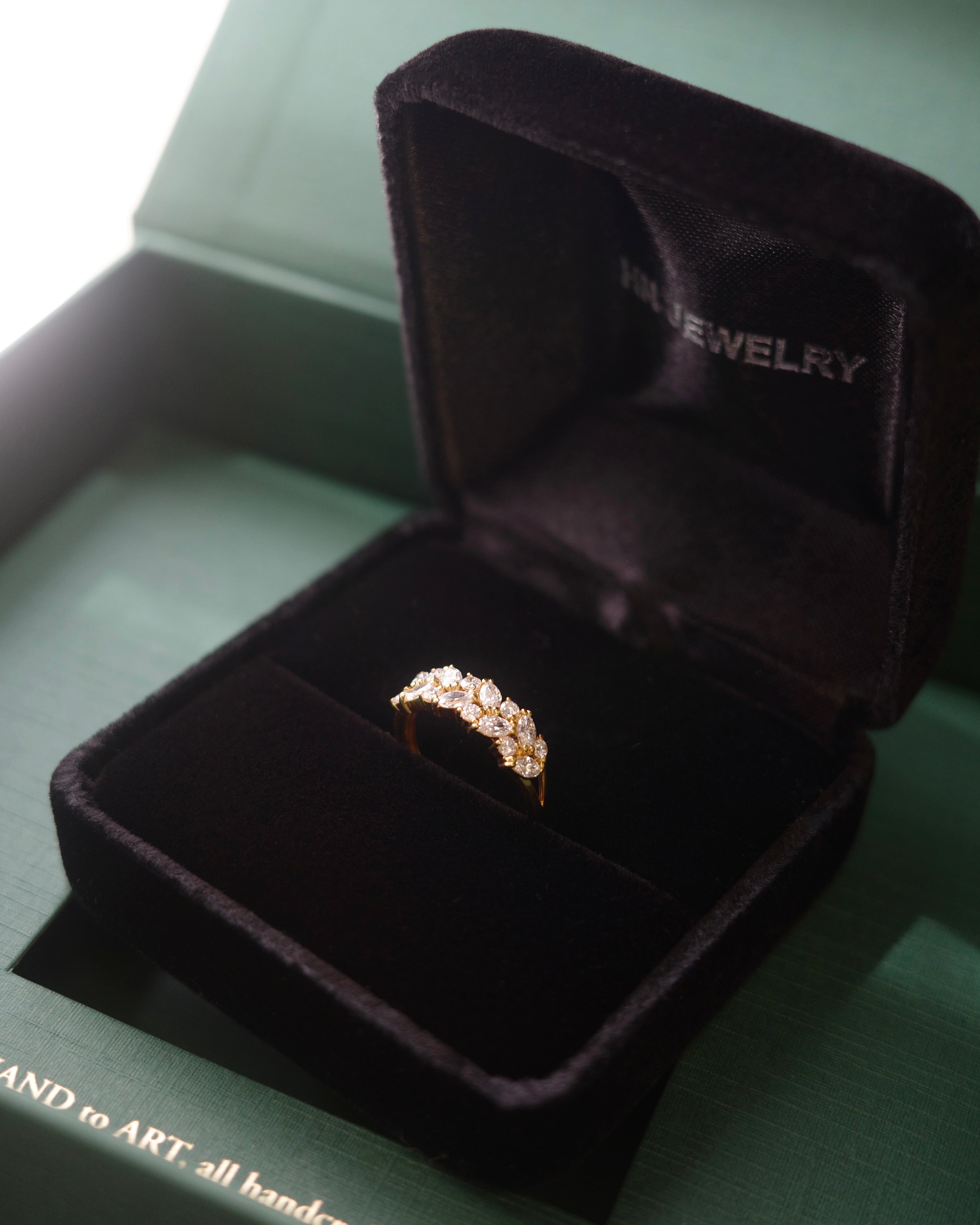marquise cut and round brilliant cut diamond wedding ring in a black velvet ring box inside a green jewelry box.
