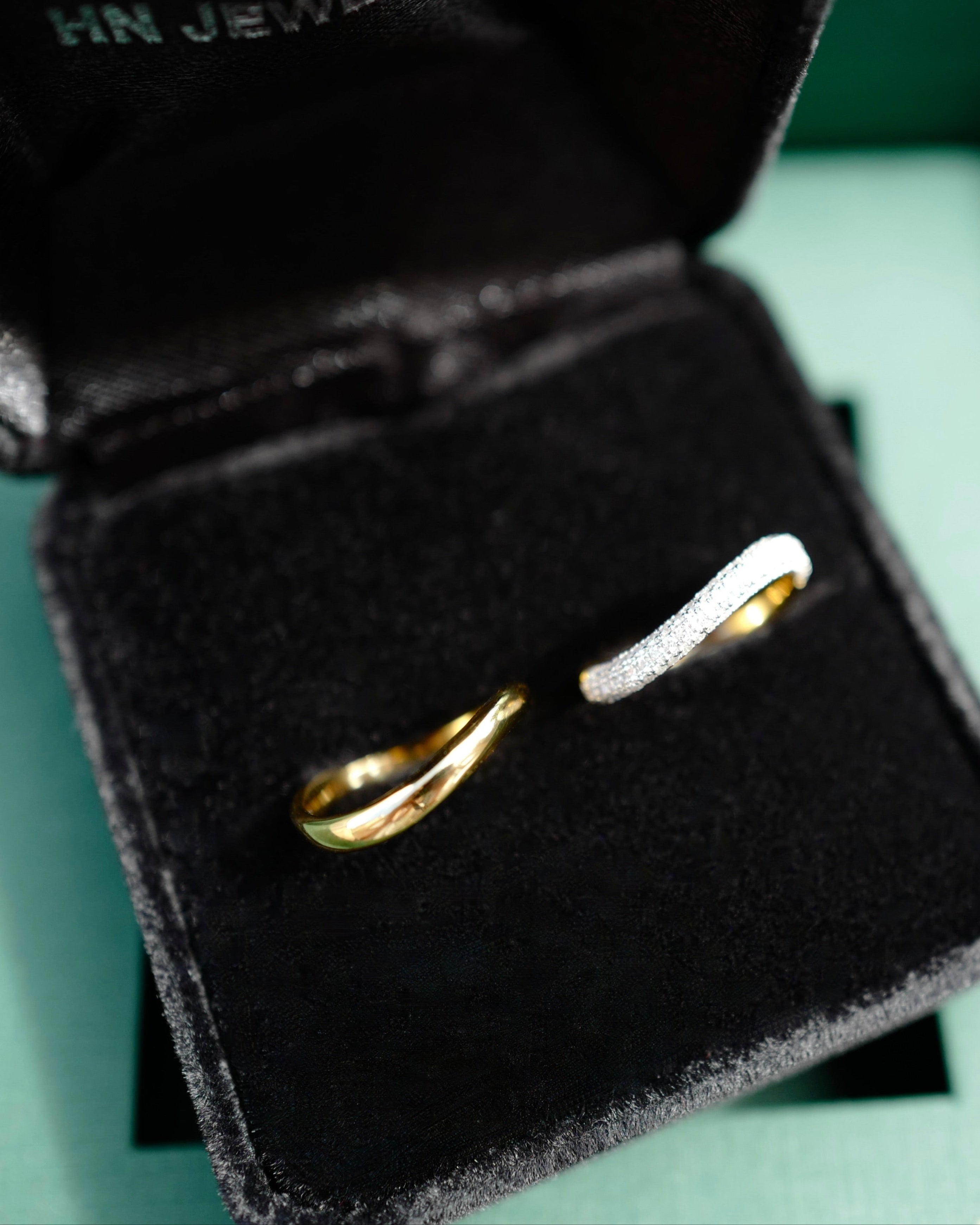 Gold wedding ring set in a black jewelry box with 'HN Jewelry' branding on a green background.