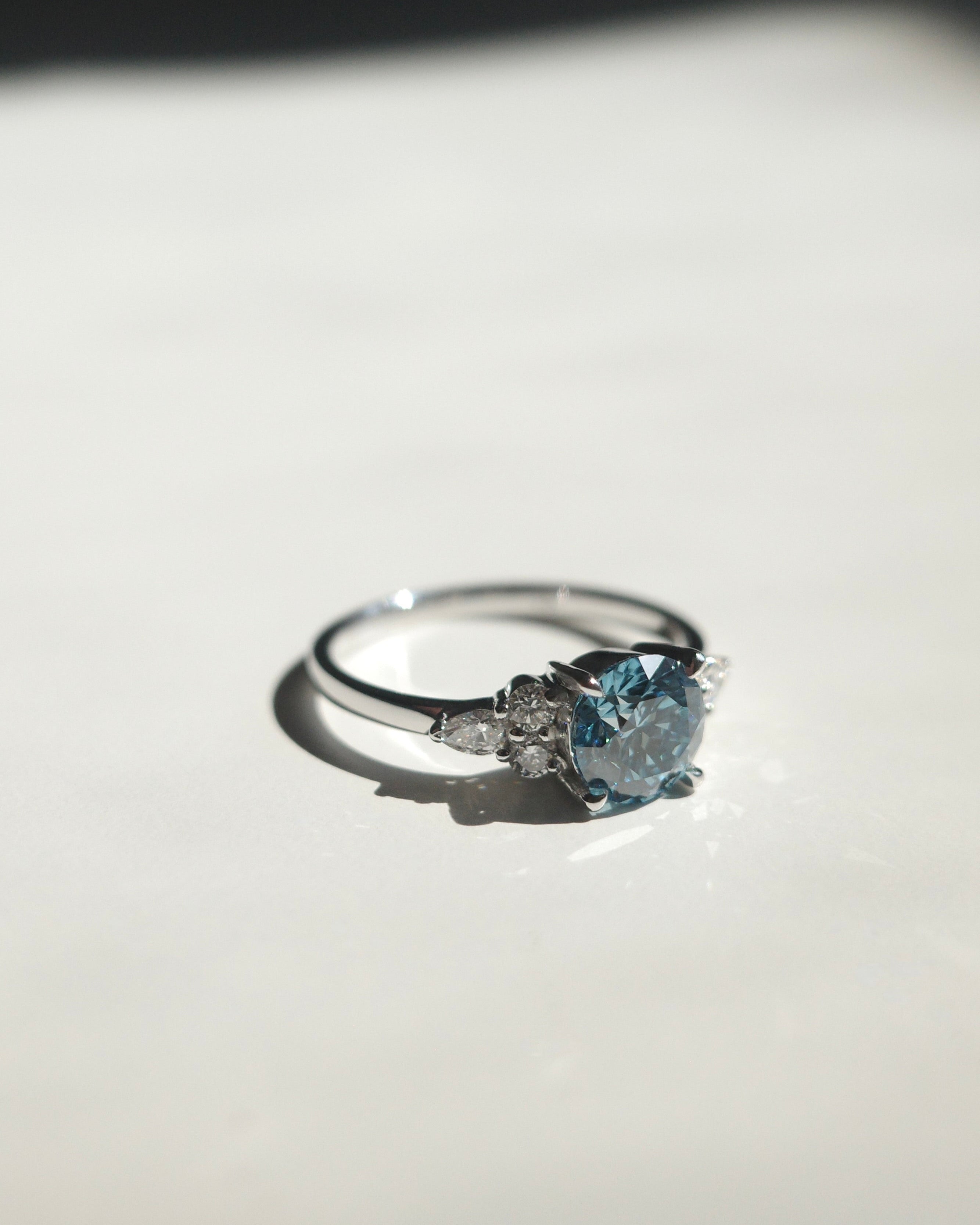white gold engagement ring with round blue diamond at the center along with pear and round diamonds on the side