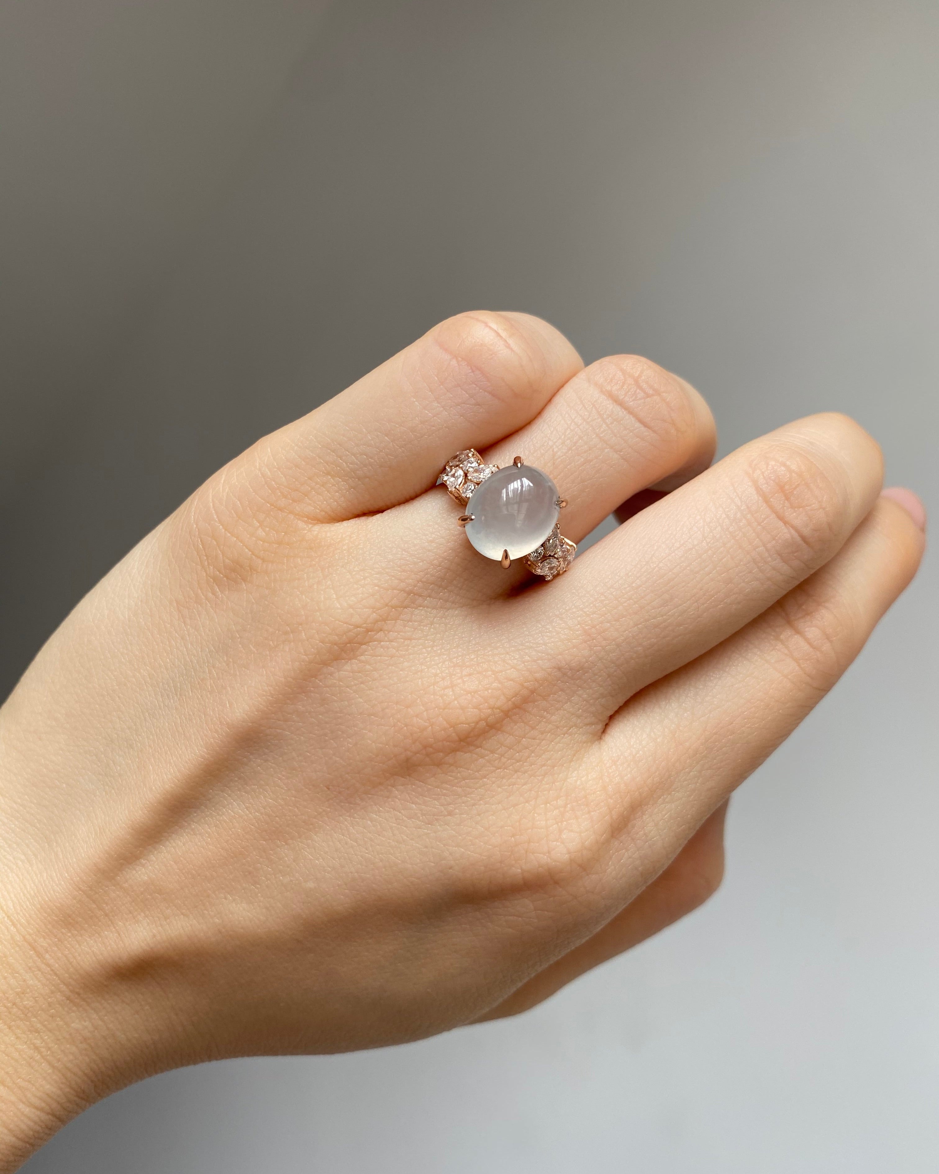 Hand wearing a ring with a natural oval icy white jade at the center and marquise diamonds on the side in 14k solid rose gold