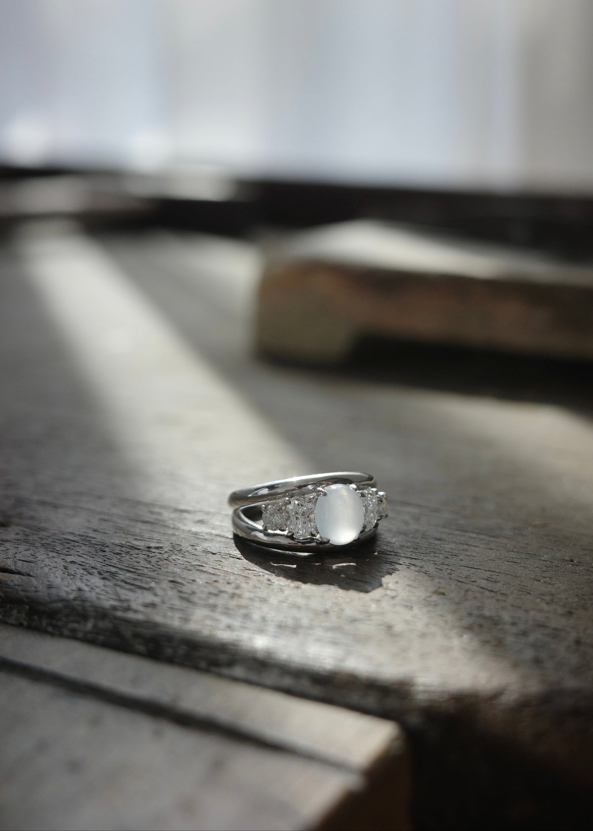 Side angle view of icy white jadeite ring showing oval and round accent diamonds on jewelry workshop table.