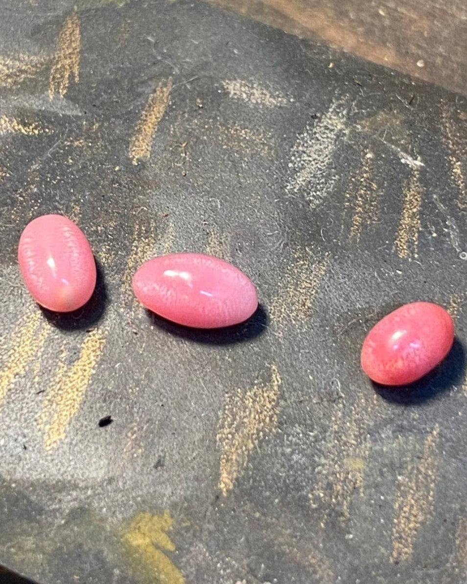 Three pink conch pearls on a textured surface