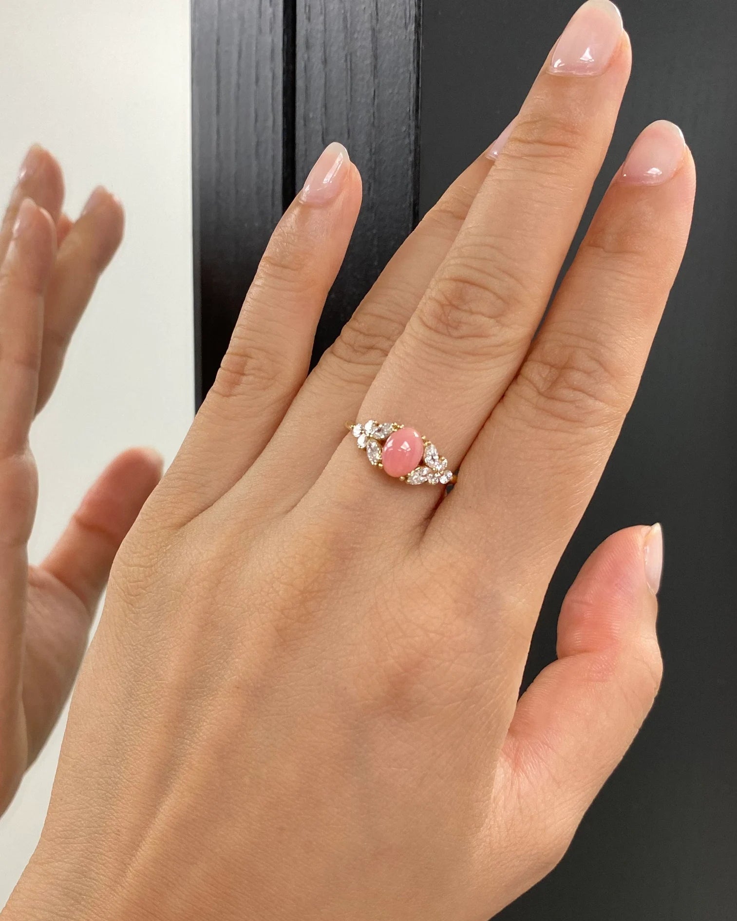 Hand wearing a ring with a pink gemstone against a neutral background