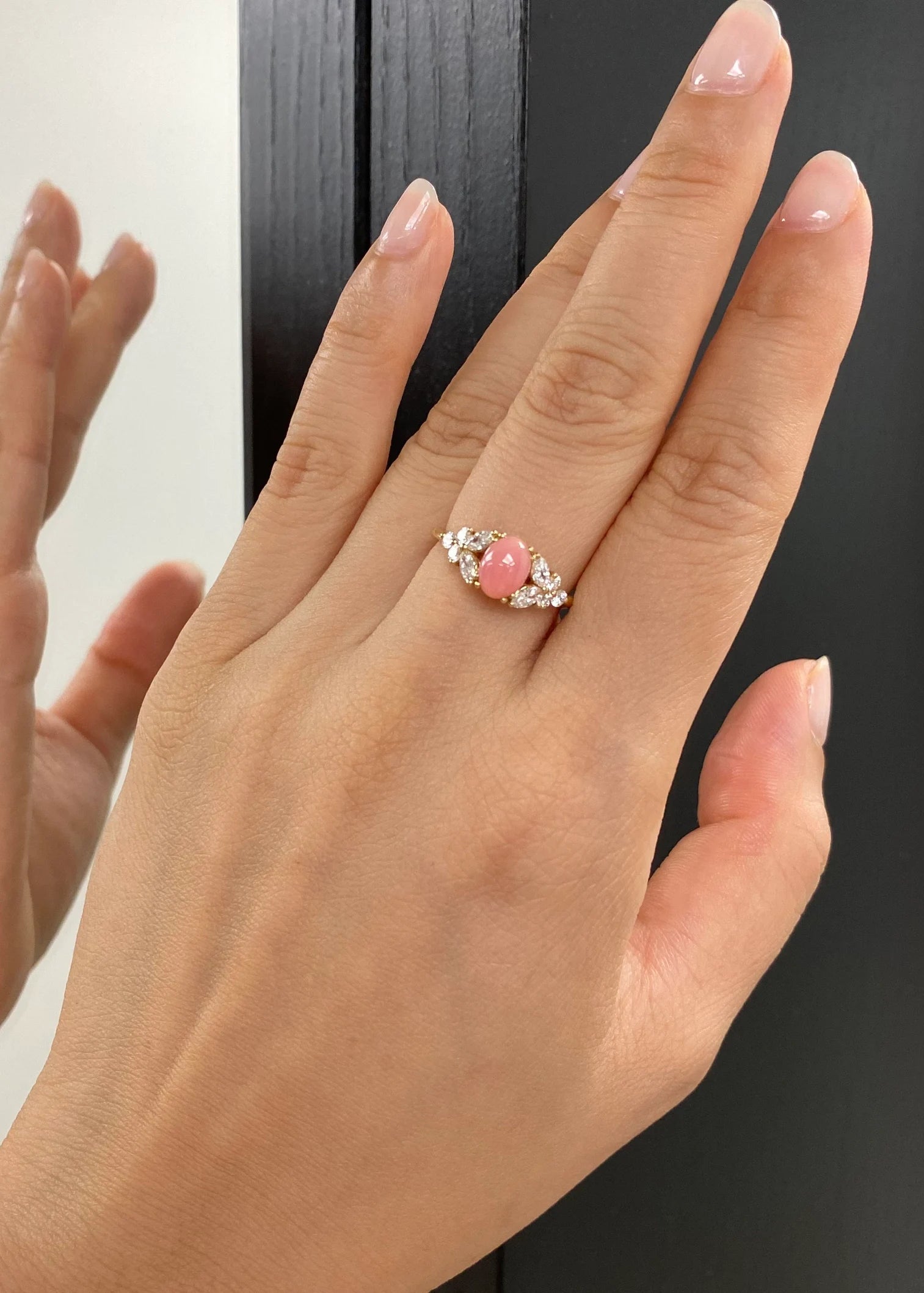 Hand wearing a ring with a pink gemstone against a neutral background