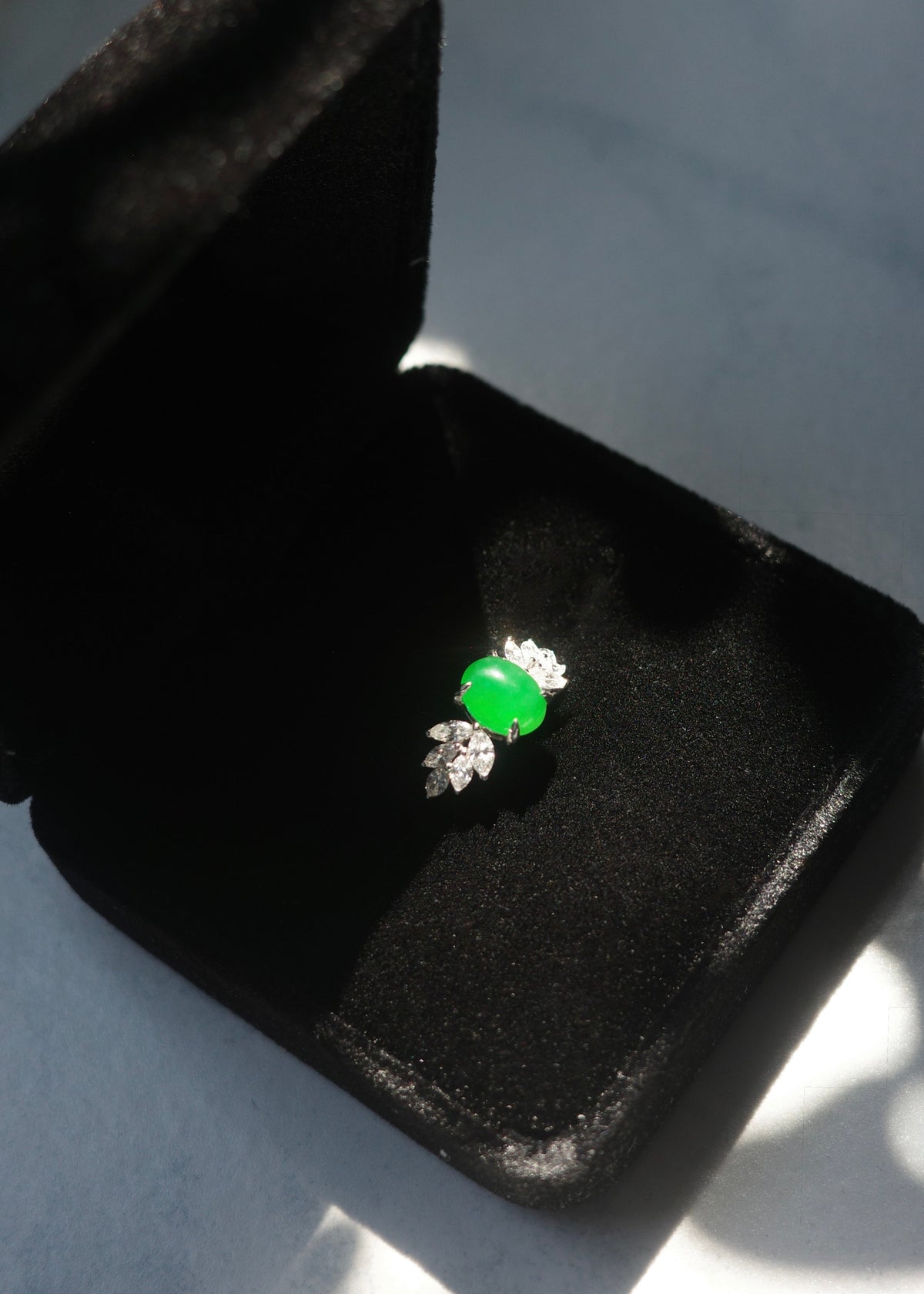 A natural green jade ring with a marquise diamond stones, displayed inside an open black velvet jewelry box.