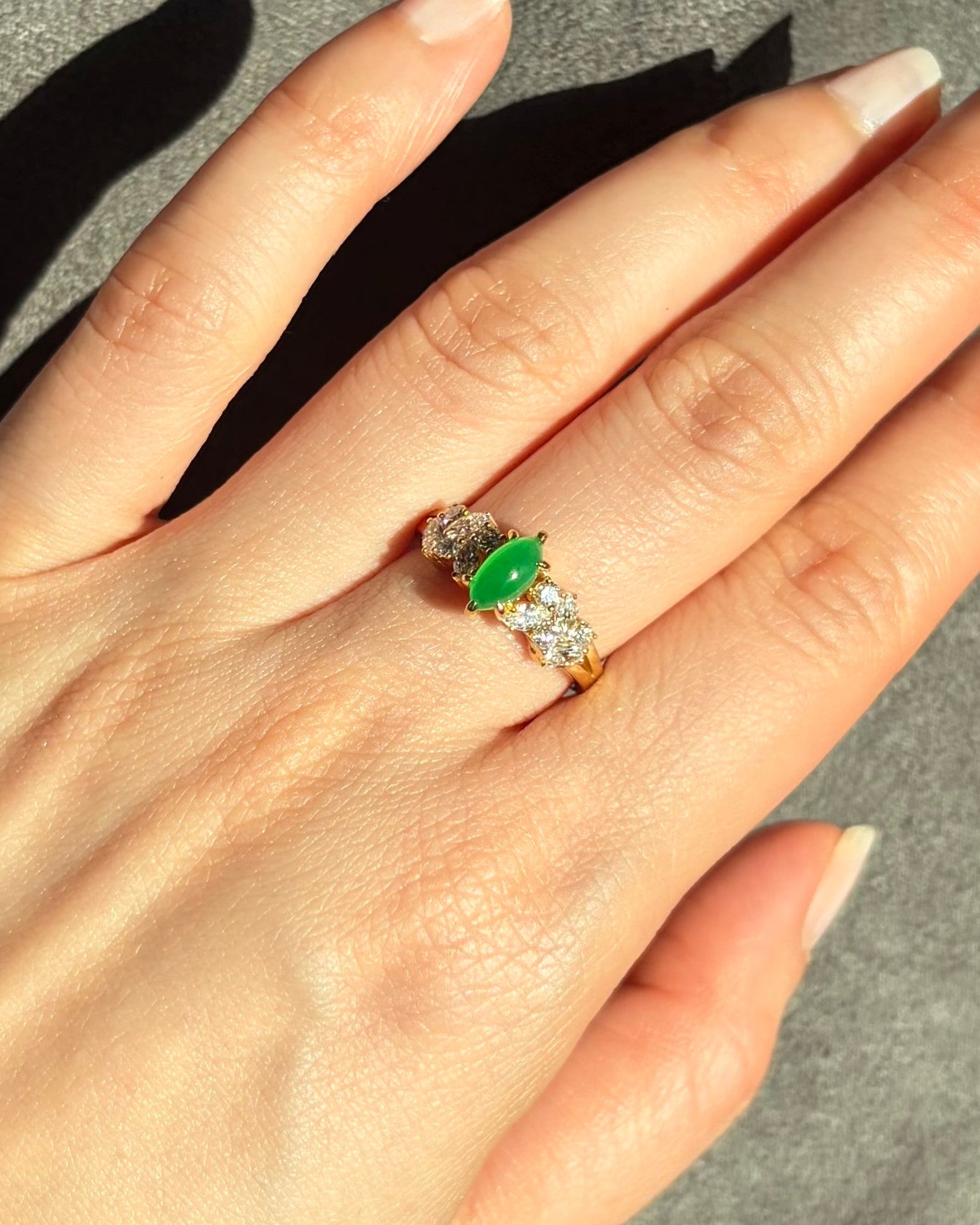 Hand wearing a ring with a marquise natural green jade on a neutral background