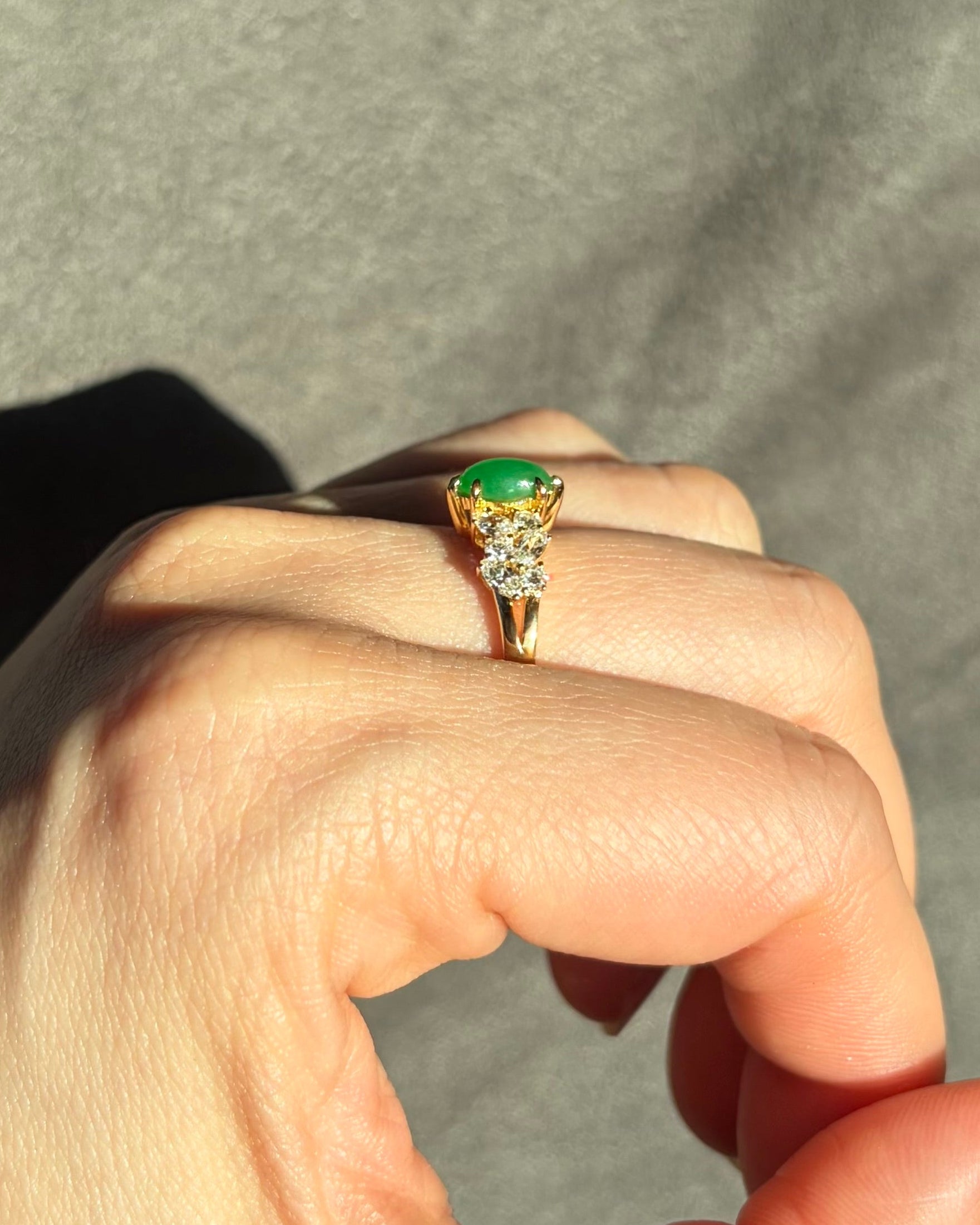 Gold ring with a green jade on a person's finger against a neutral background