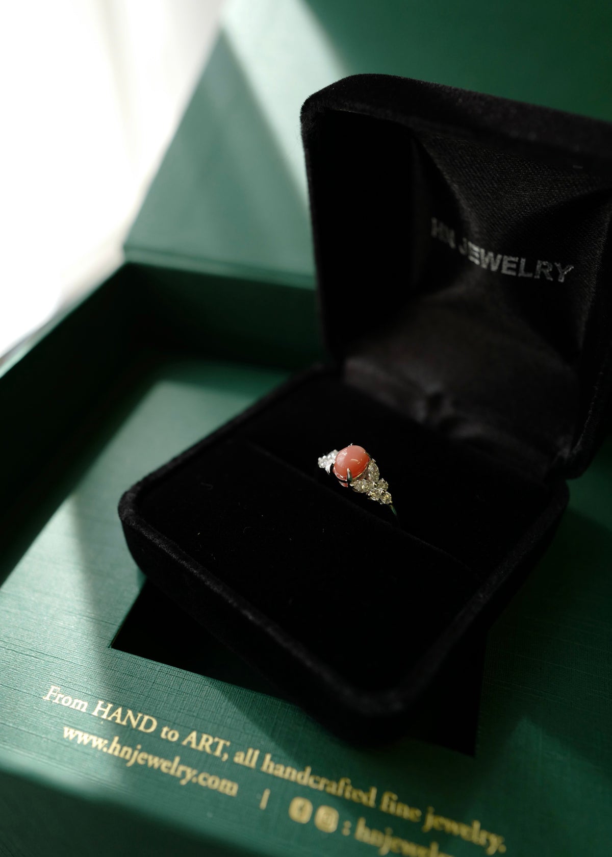 A gold ring with a conch pearl set in a black velvet jewelry box, placed on a green branded HN Jewelry box.