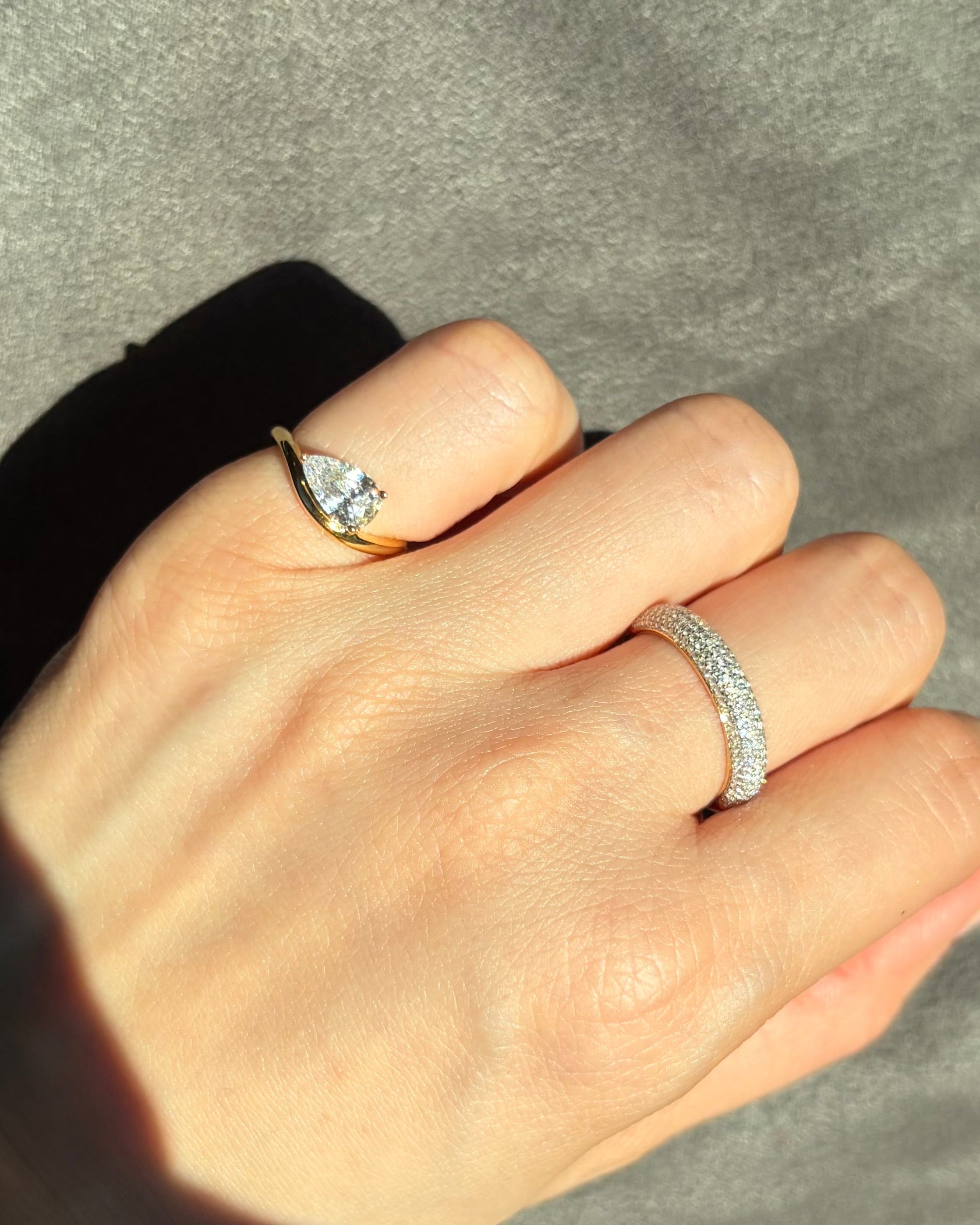 Hand wearing two rings on a neutral background