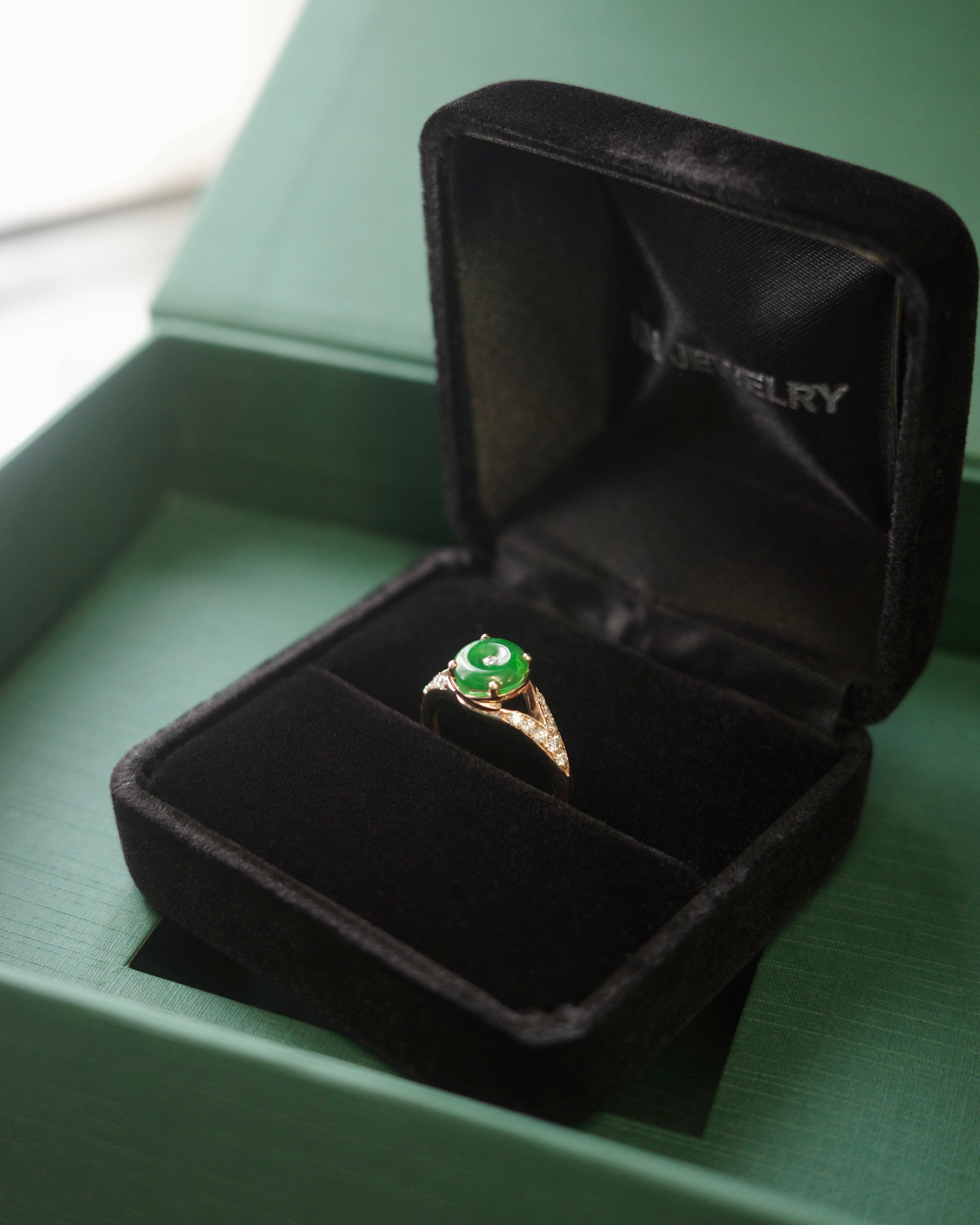 Rose gold ring with a green circle jade in an open ring box on a green packaging box