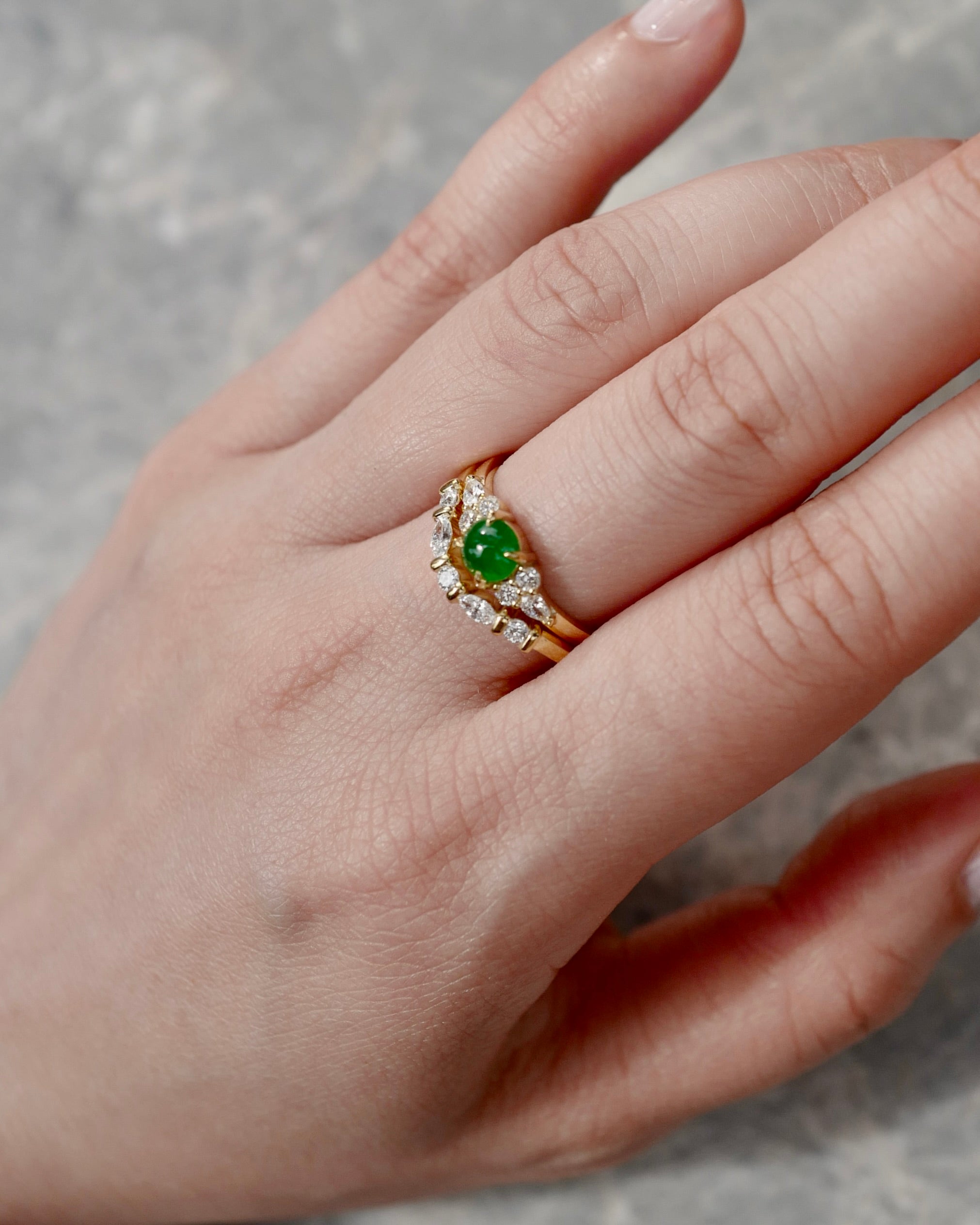 Hand wearing a yellow gold engagement ring with a natural green jade on a neutral background