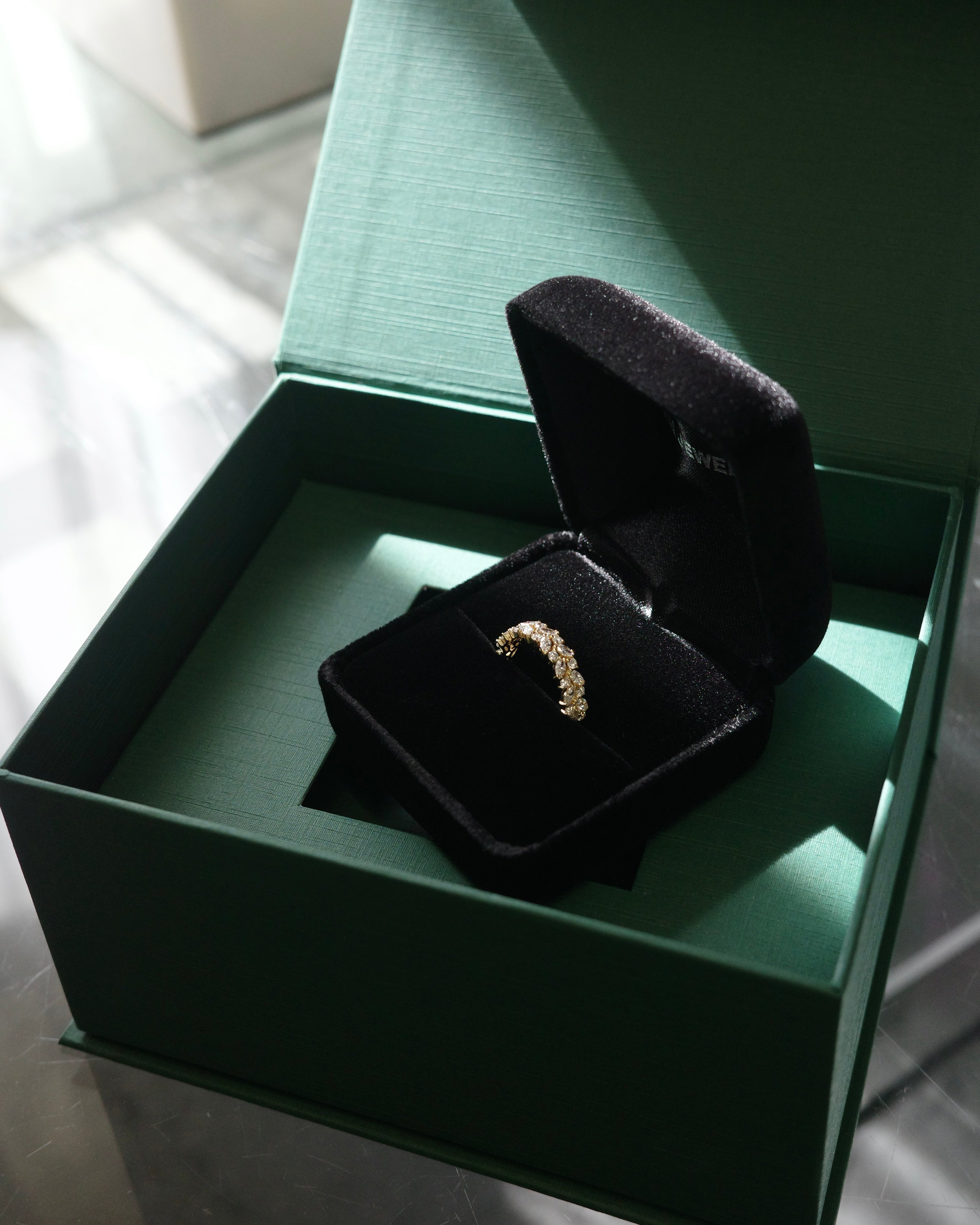 marquise cut and round brilliant cut diamond half eternity wedding ring in a black velvet ring box inside a green jewelry box.