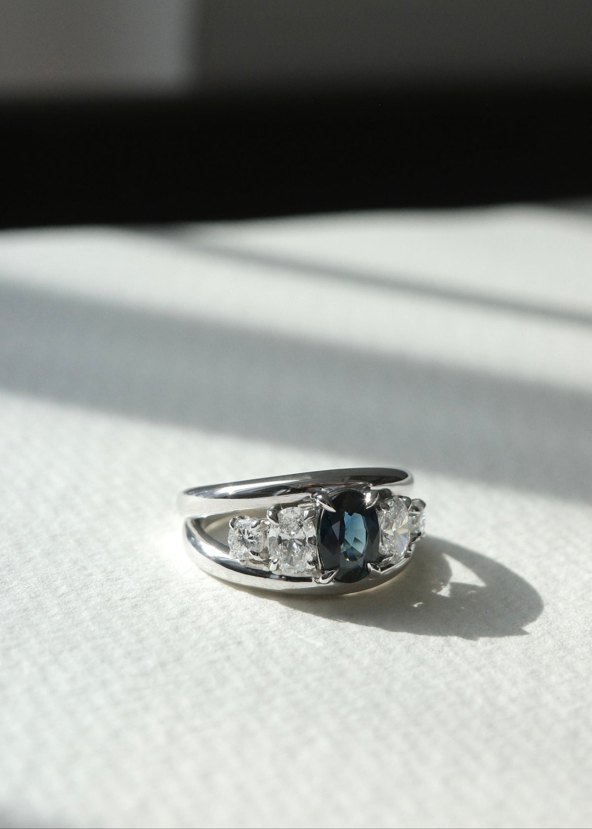 Studio shadow view highlighting the raised five-stone cluster of teal sapphire and diamonds.