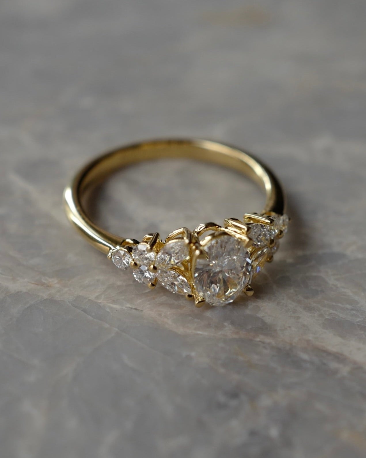 Gold ring with oval cut diamonds at the center along with marquise cut diamonds on a marble stone table. 