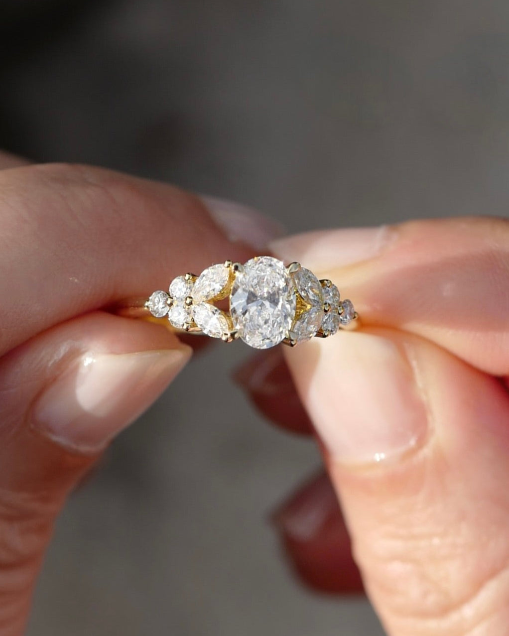 An oval diamond gold engagement ring held between fingers 