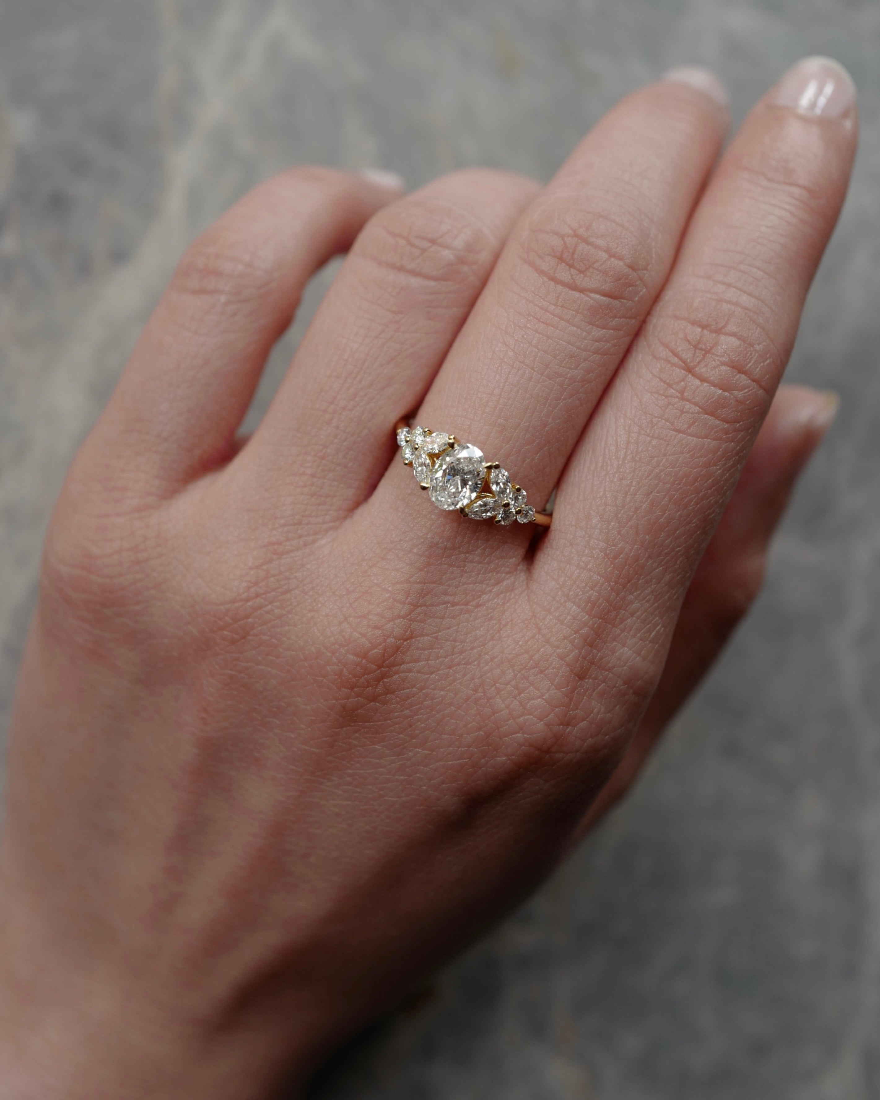 Hand wearing a oval cut diamond ring at the center along with marquise and round diamonds on the side