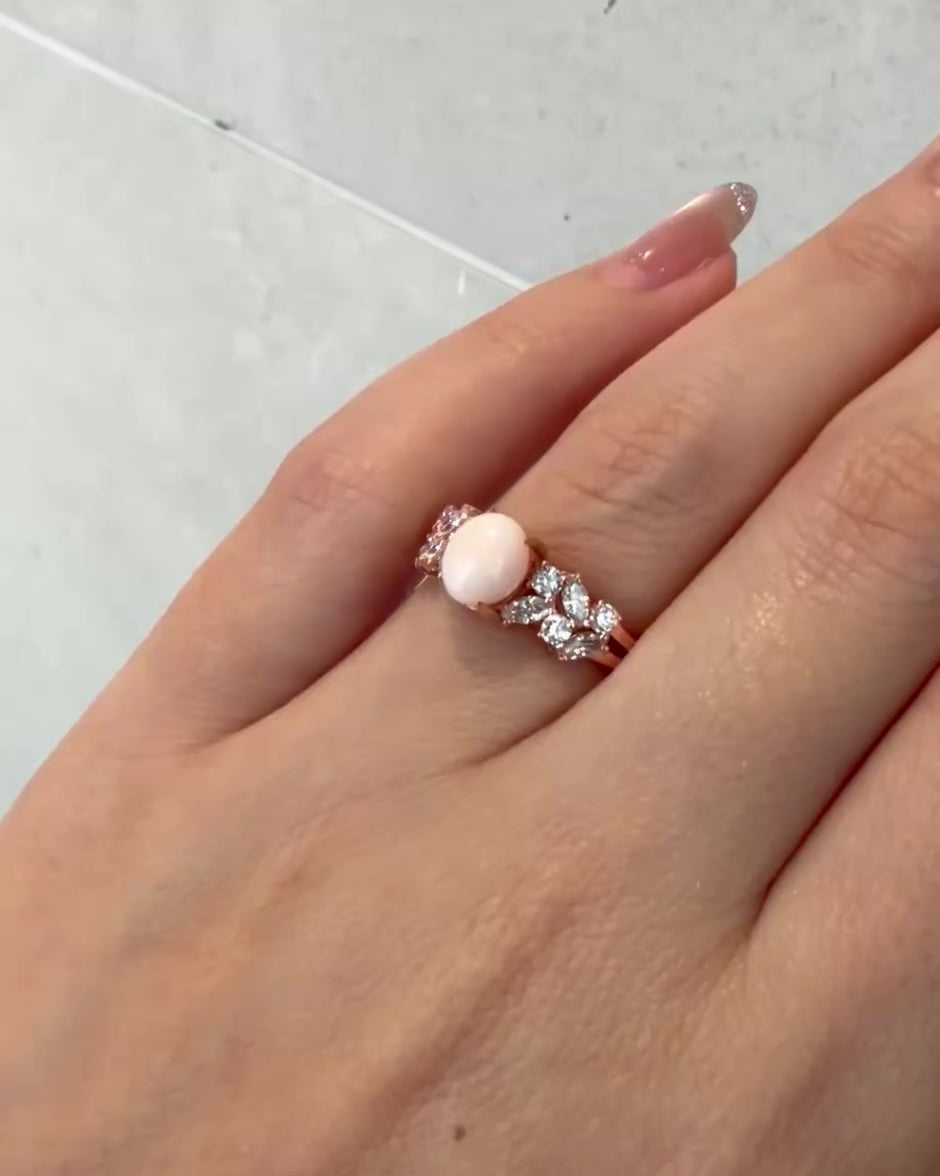 An engagement ring set with oval natural white pink conch pearl along with marquise diamonds and round brilliant cut diamonds on the side. 