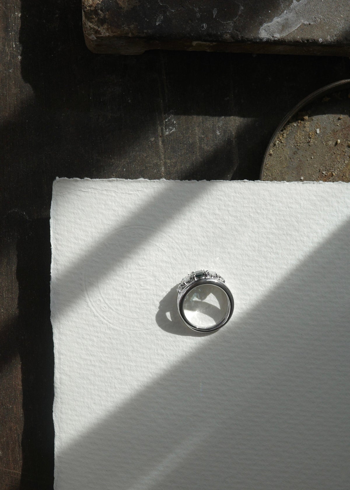 Top-down view of five-stone natural teal sapphire ring flanked by oval and round brilliant diamonds.