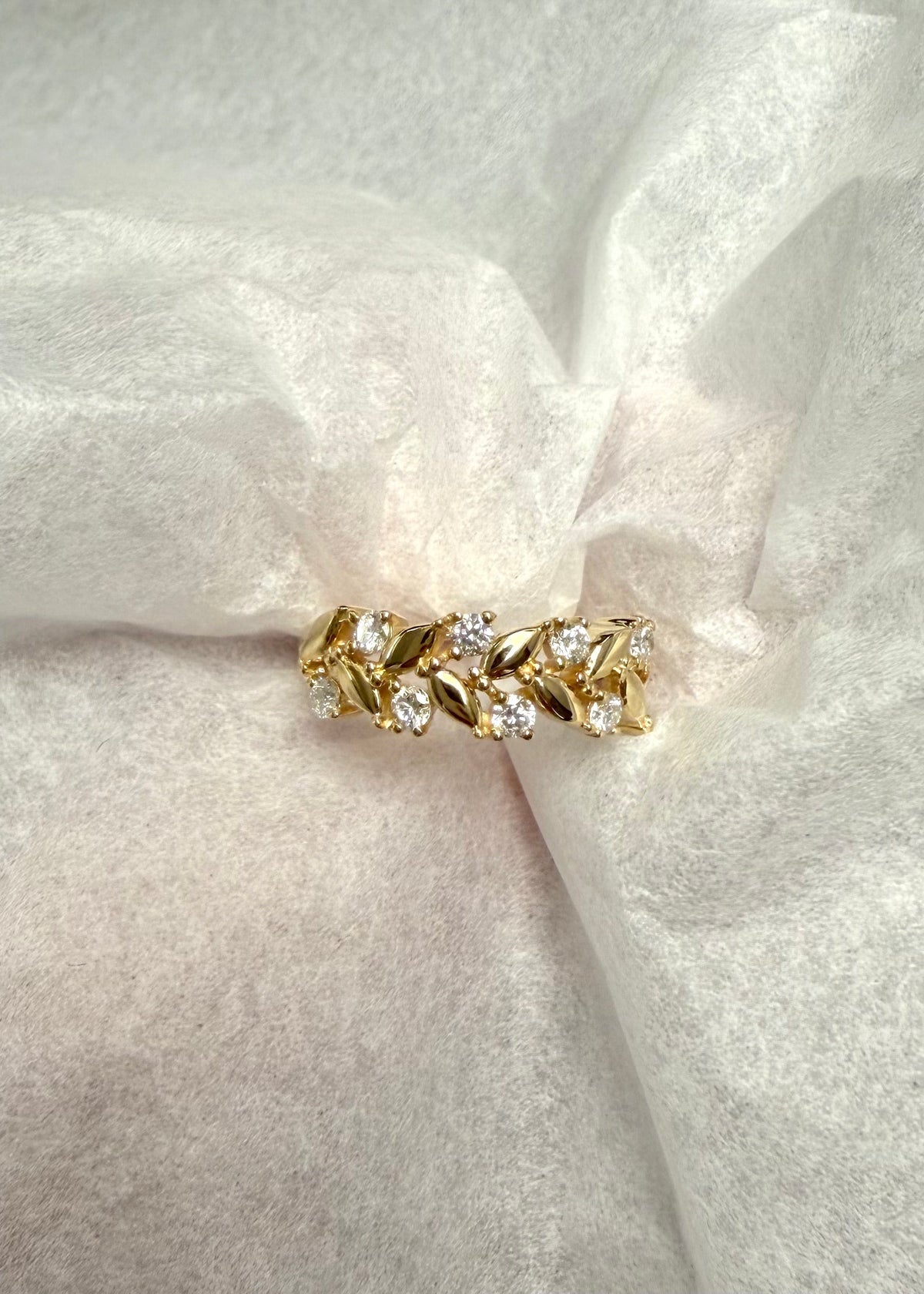 A gold leaf-patterned ring with clear marquise-cut gold pattern, displayed on a textured white fabric background.