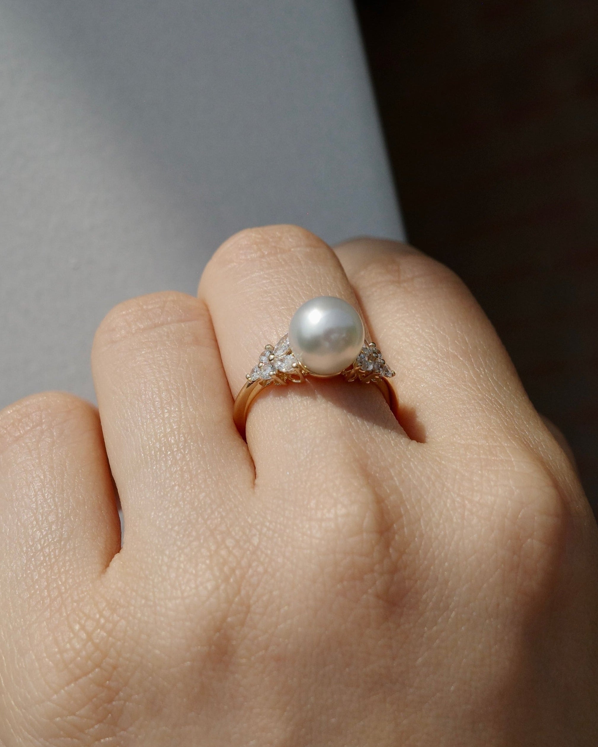 Hand wearing a south sea round pearl and marquise diamonds ring on a neutral background